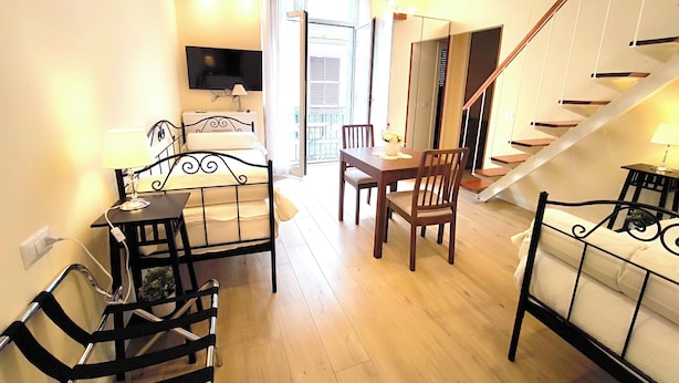 A bedroom with a bed, bedside table, lamp, TV, and a balcony with a table and chairs. - Agorà Rooms (Naples)