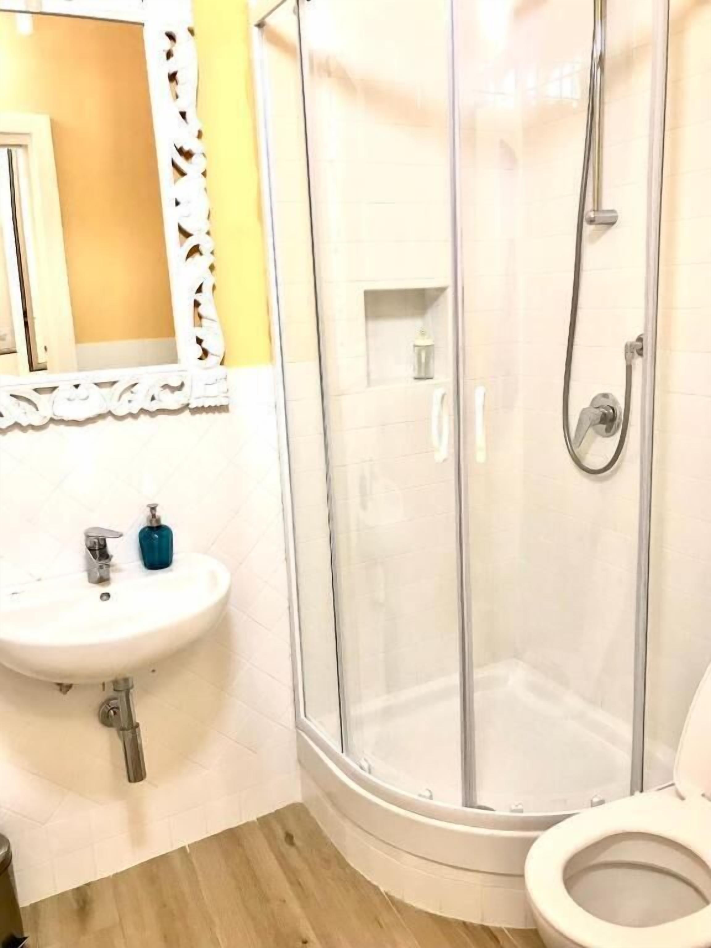 Un baño con ducha, inodoro, lavamanos y un espejo con marco decorativo.