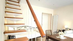 A staircase leading to a bedroom with a bed, a dining table with chairs, and a lamp. - Agorà Rooms (Naples)