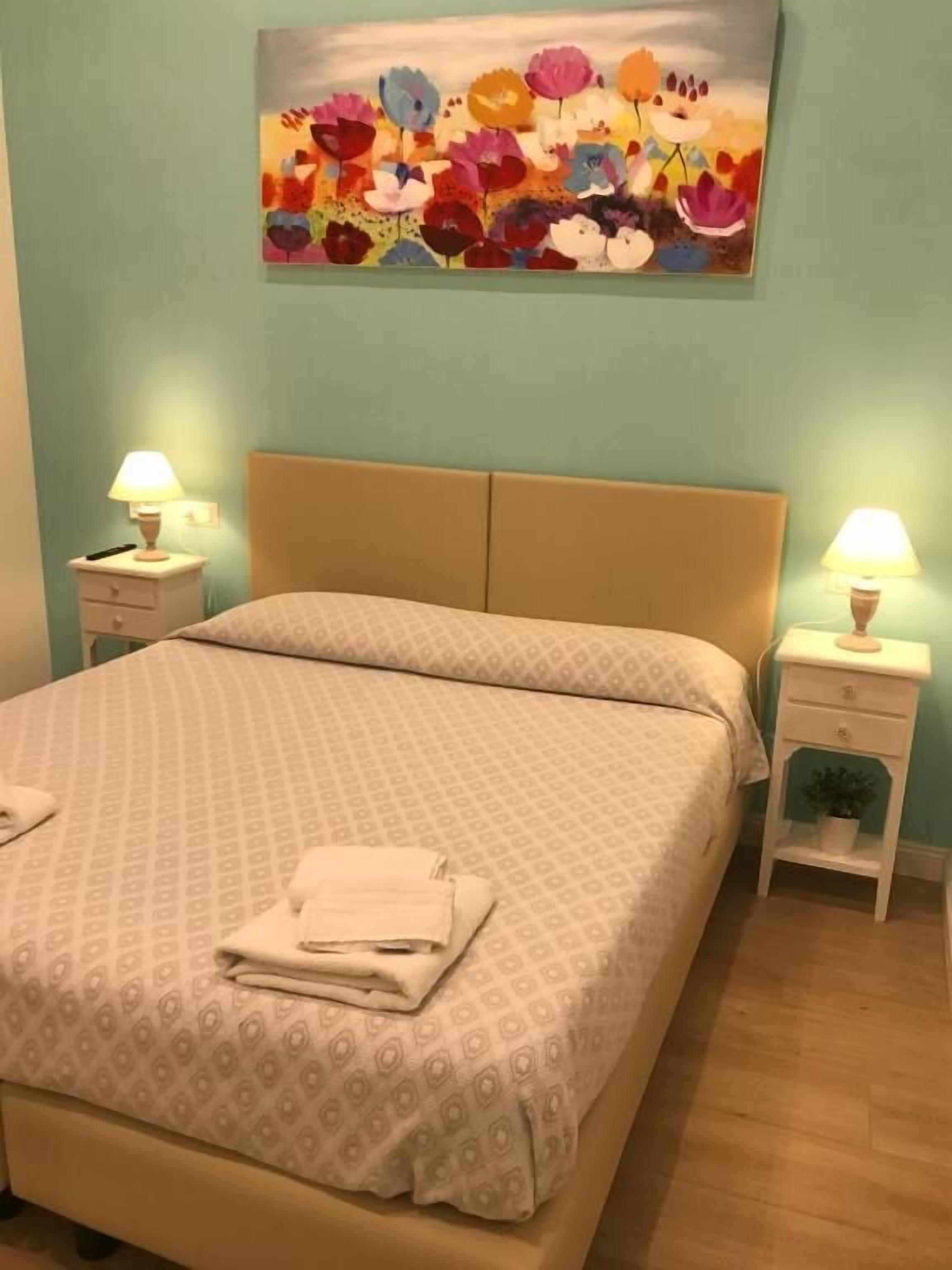 Une chambre à coucher avec un lit, deux tables de chevet avec des lampes, un tableau mural et une petite plante.