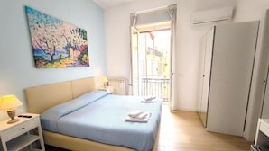 A bedroom with a bed, bedside table, lamp, painting, and a view of the outside. - Agorà Rooms (Naples)