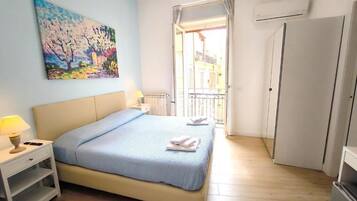 Ein Schlafzimmer mit Bett, Nachttisch, Lampe, Gemälde und Blick ins Freie.