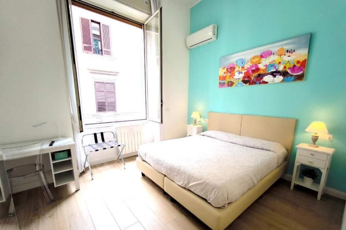 A bedroom with a bed, bedside tables, a desk, and a window with shutters.