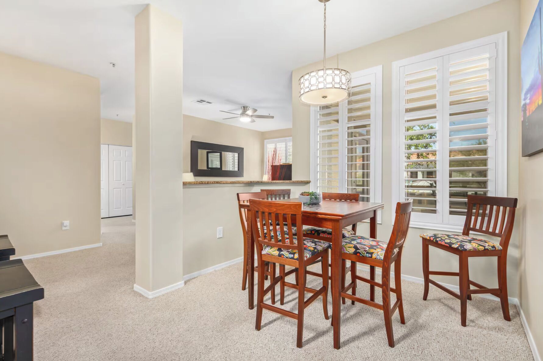 A dining area with a wooden table and chairs, a ceiling fan, and a window with blinds.