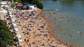 A crowded beach with numerous people and tents, a bridge in the background, and a cityscape. - 1,001 Wonders (Fénay)