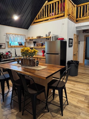 A kitchen with a wooden table, chairs, a refrigerator, and a window with a view.