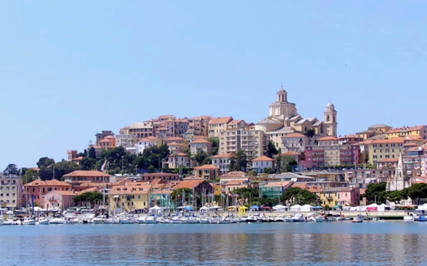 A coastal cityscape with buildings, a prominent dome structure, and a marina with boats.
