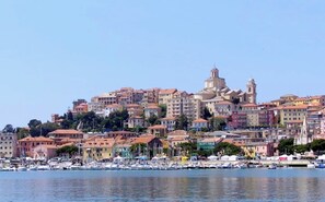 A coastal cityscape with buildings, a prominent dome structure, and a marina with boats. - Casa dell'Arte ArtGarage (Imperia)