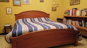 Ein Bett mit gestreifter Decke, ein Holzkopfstück, ein Nachttisch, eine kleine Lampe und ein Bücherregal mit Büchern.
