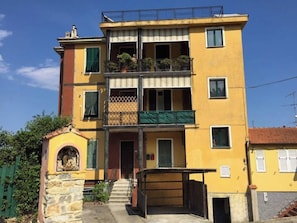 A multi-story yellow building with balconies, a stone entrance, and a visible staircase leading to the entrance. - Casa dell'Arte ArtGarage (Imperia)