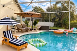 Ein Poolbereich mit Liegestühlen, einem Sonnenschirm und aufblasbaren Schwimmringen.