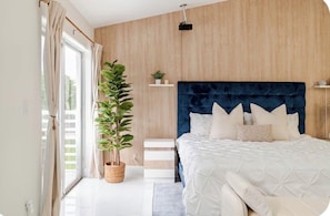 A bedroom with a large bed, a wooden wall, a potted plant, and a window with curtains.