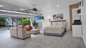 Un dormitorio moderno con cama, sofá, mesa de centro, televisor y proyector instalado en el techo.