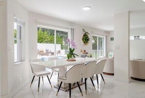 A modern dining area with a glass table and white chairs, a hanging plant, and a view of the outdoors.