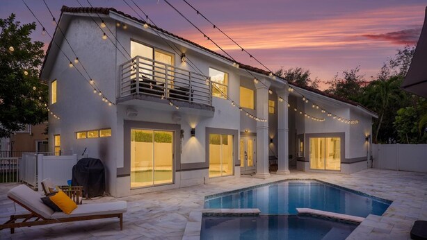 Una casa moderna con piscina, ventanas amplias y luces colgantes.