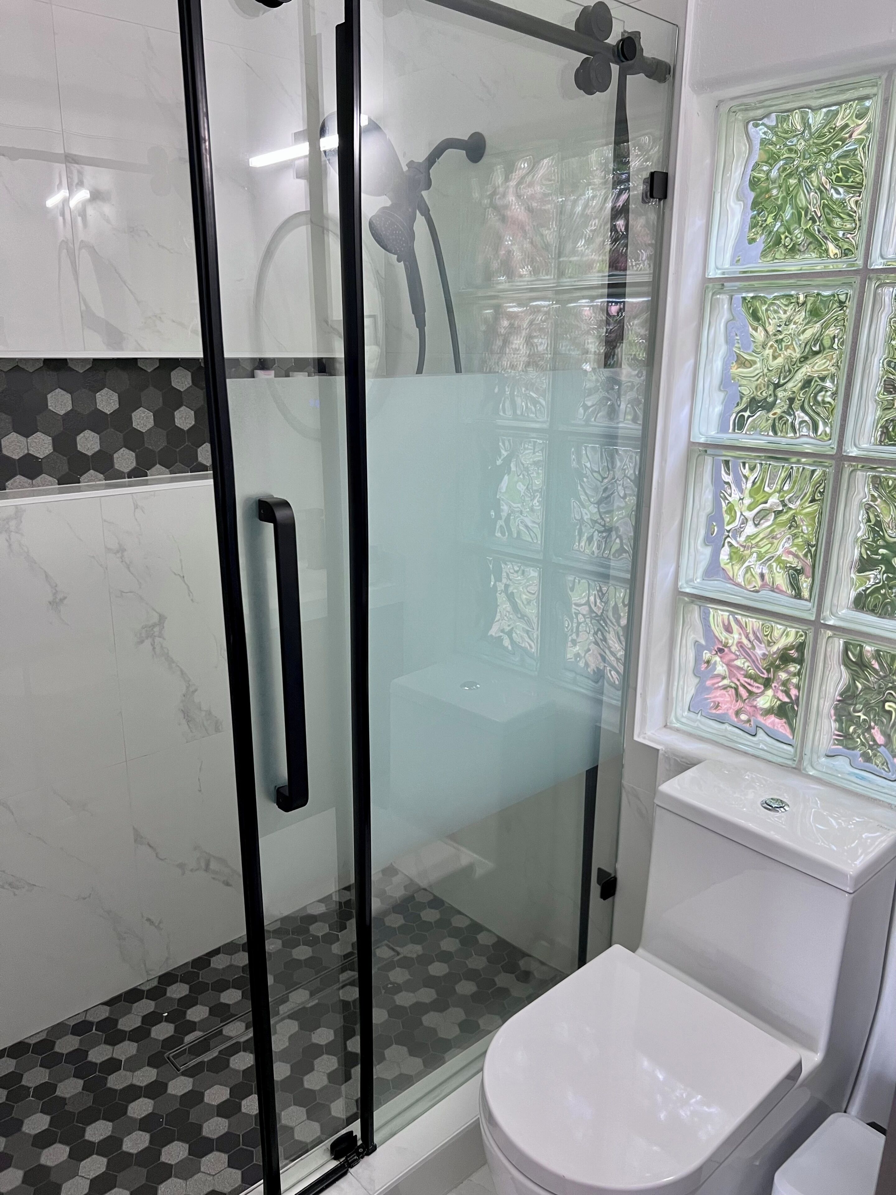 A modern bathroom with a glass-enclosed shower, a toilet, and a window with decorative glass panes.