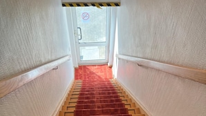 A carpeted stairway with a handrail, leading to a door with a no-smoking sign.