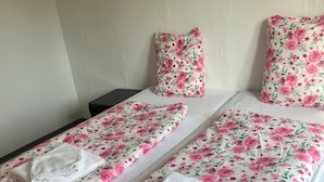 A hotel room with two beds, floral bedding, white towels, and a painting of flowers on the wall.
