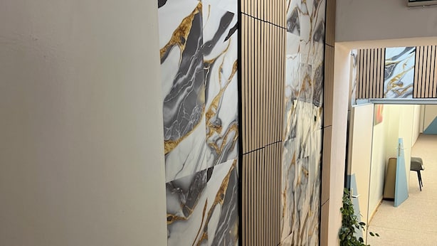 A hallway with a marble-patterned wall, a wooden floor, and a door with a handle.