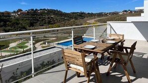 Terraço no telhado com piscina, mesa de jantar e cadeiras, com vista para uma paisagem montanhosa.