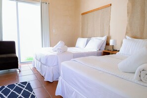 Habitación de hotel con dos camas, una silla, una lámpara y vistas por la ventana.