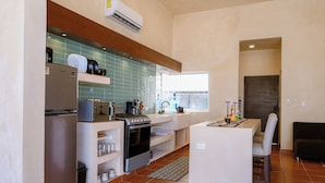 A compact kitchen with a refrigerator, stove, microwave, and a small dining area with a chair. - Casa Akna Chicxulub by Casago (Chicxulub)