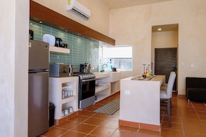 Una cocina compacta equipada con refrigerador, estufa, microondas y una pequeña zona de comedor con una silla.