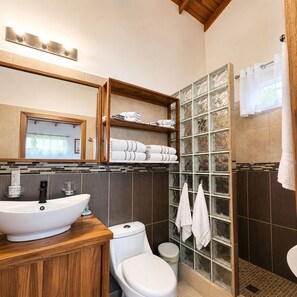 A bathroom with a wooden vanity, a white sink, a toilet, a glass shower enclosure, and a towel rack. - Terra Chula 1BR Bungalow with Ocean & Nature Views (Roatán)