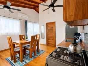 A kitchen with wooden cabinets, a gas stove, and a dining area with a table and chairs. - Terra Chula 1BR Bungalow with Ocean & Nature Views (Roatán)