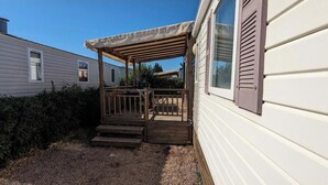 Eine überdachte Veranda mit Stufen, die zu einer Holzterrasse führen, neben einem weißen Haus mit braunen Fensterläden.