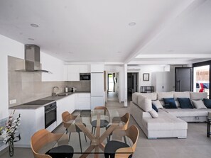 A modern kitchen with white cabinets, a dining table with chairs, and a living area with a sofa and cushions. - Sand, Sea and Love by Interhome (Puerto Rico)