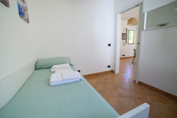 A bedroom with a bed, a green bedspread, and a neatly folded white towel.