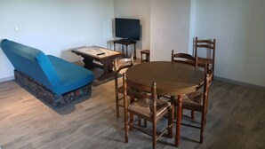 A living room with a sofa, a TV, a dining table with chairs, and a patterned rug. - Atchoum Vacation Rental (Hostun)