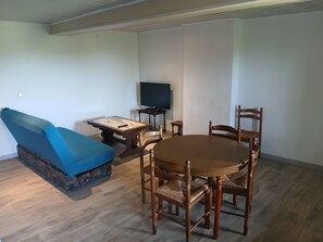 Ein Wohnzimmer mit blauem Sofa, einem Holzesstisch mit Stühlen, einem Fernseher und einem kleinen Beistelltisch.
