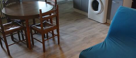 A compact living space with a dining table, chairs, a sofa, a washing machine, a microwave, and a refrigerator.