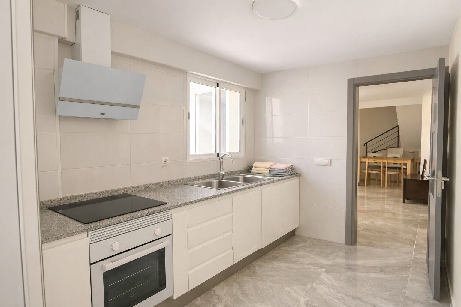 Una cocina moderna con armarios blancos, encimera de granito, horno integrado y ventana sobre el fregadero.