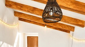 A cozy dining area with a table set for four, surrounded by wicker furniture, under a wooden beam ceiling with a hanging light fixture.