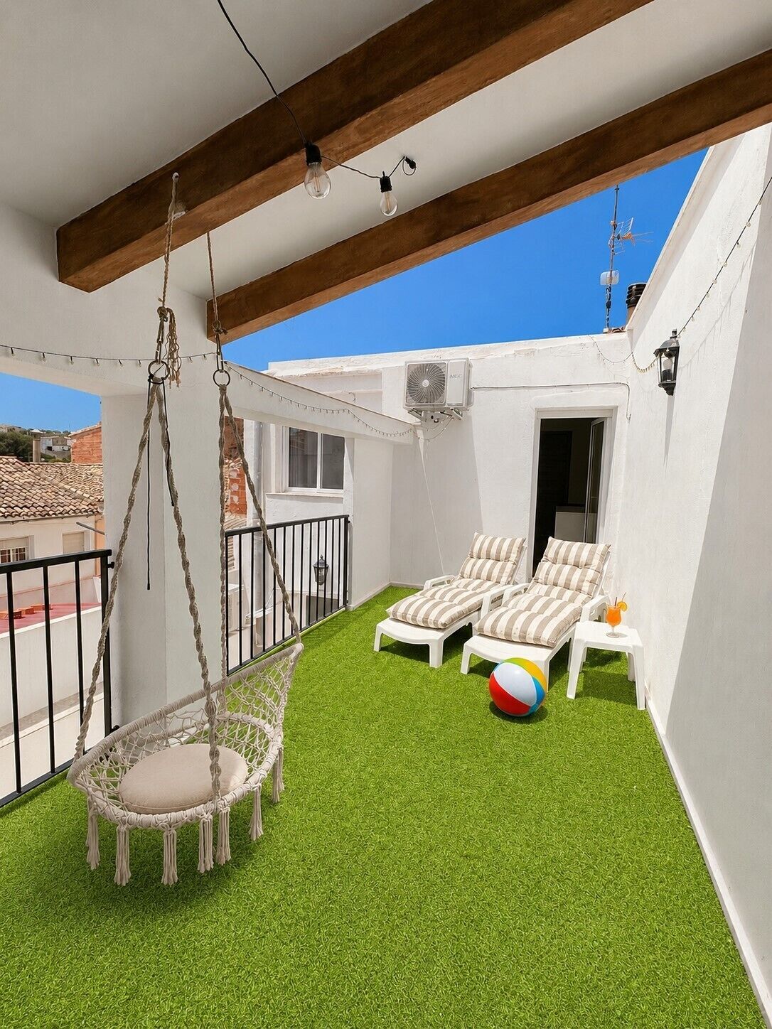 Un balcón con césped artificial, dos sillones de descanso, una silla colgante y una pelota de playa.