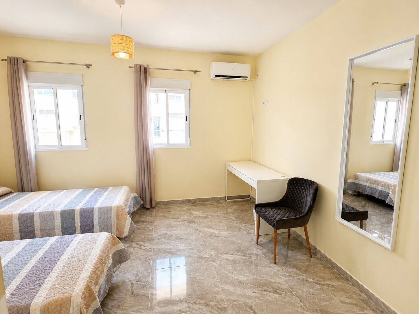 A bedroom with two beds, a desk, a chair, an air conditioning unit, and a large mirror.