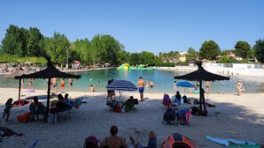 A beach with a pool, umbrellas, and people.