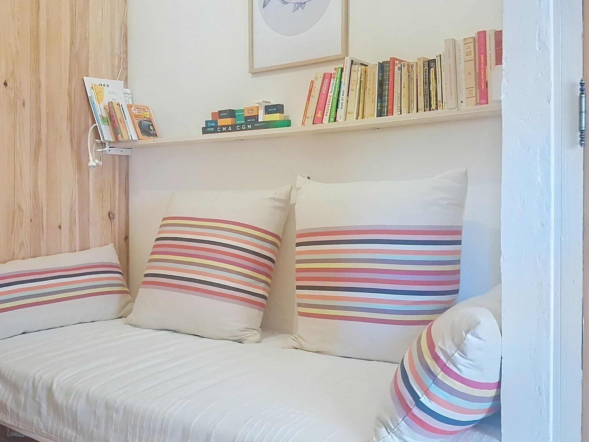 A room with a sofa, striped pillows, a bookshelf with books, and a framed picture on the wall.