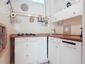 A compact kitchen with white cabinets, a wooden countertop, a gas stove, a sink, and a clock on the wall. - Le Weekend by Interhome (Saint Cyr sur mer Les Lecques)