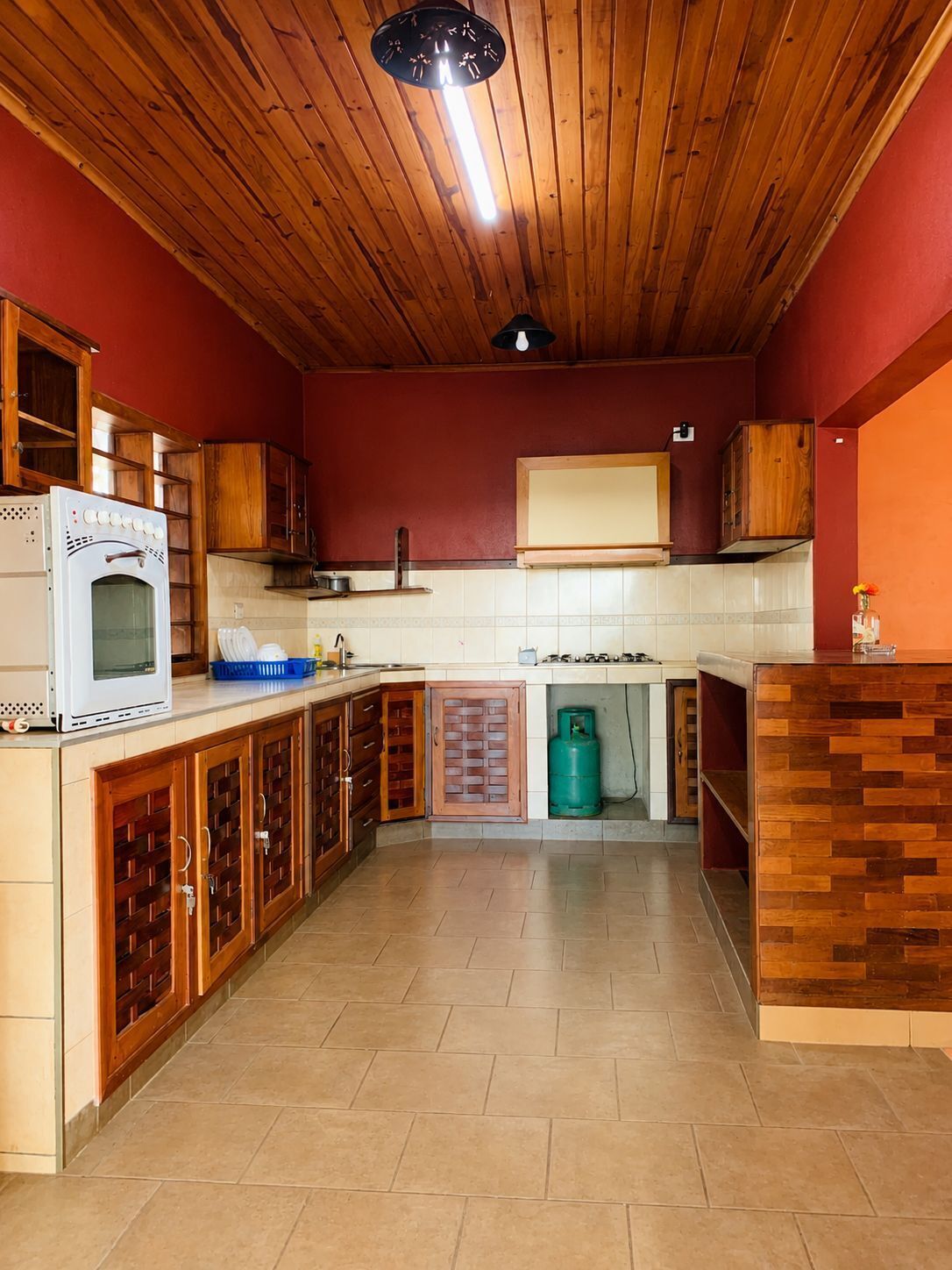 Una cocina con armarios de madera, un horno blanco, una estufa a gas y un cilindro de gas verde.