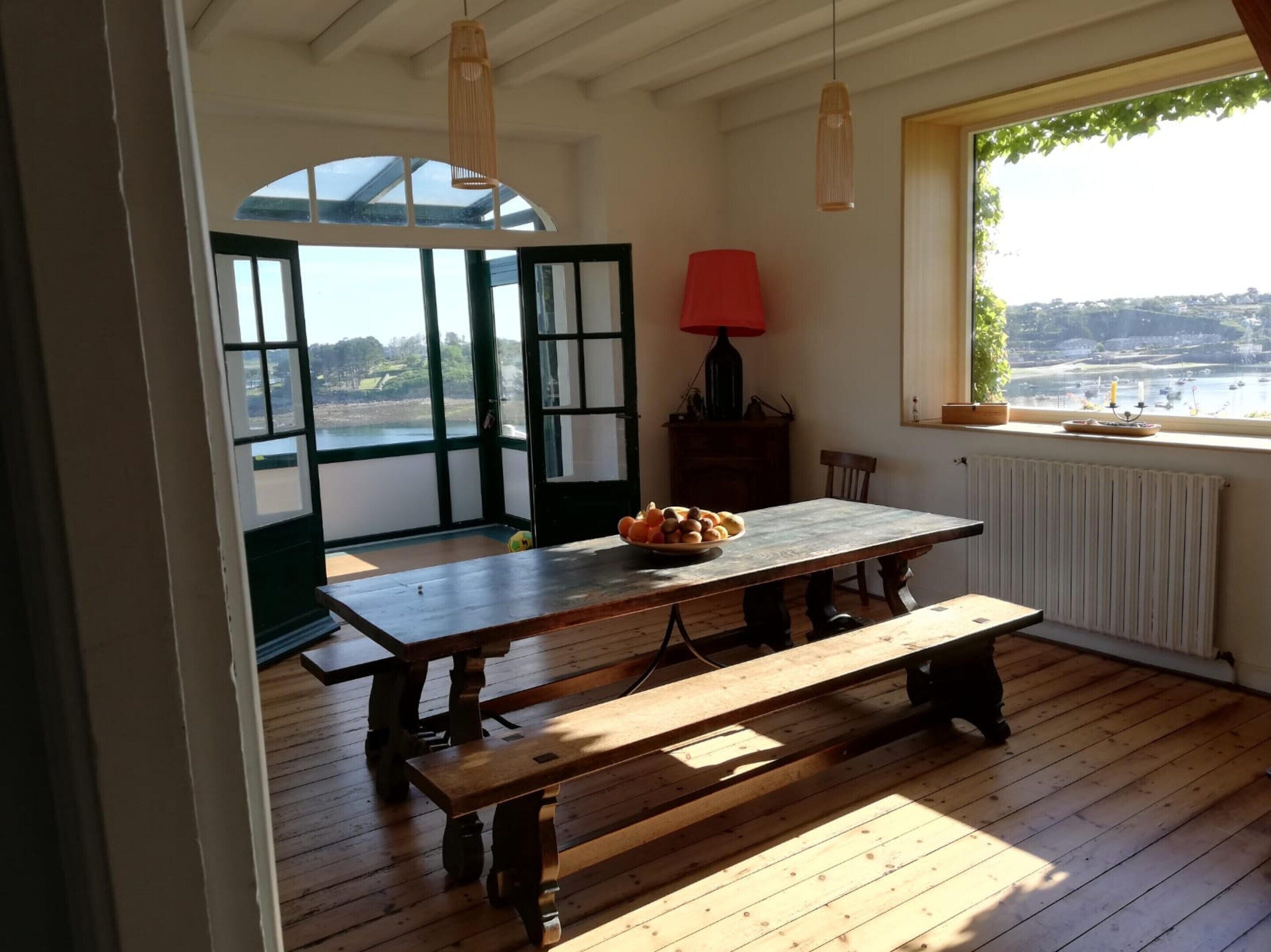 A wooden dining table with benches in a room with a view of a body of water through large windows.