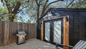 A wooden deck with a grill, a wooden chair, and a black building with large windows. - Tech Terrace Retreat - TTU, J&B Coffee, Brewery (Lubbock)