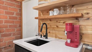 A kitchen with a sink, a coffee maker, and a shelf with dishes and glasses. - Tech Terrace Retreat - TTU, J&B Coffee, Brewery (Lubbock)
