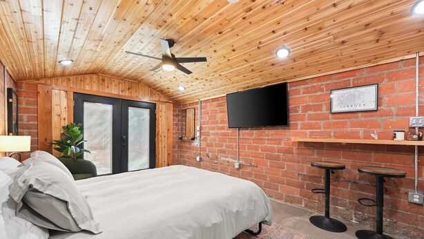A bedroom with a bed, a ceiling fan, a TV, and a brick wall. - Tech Terrace Retreat - TTU, J&B Coffee, Brewery (Lubbock)