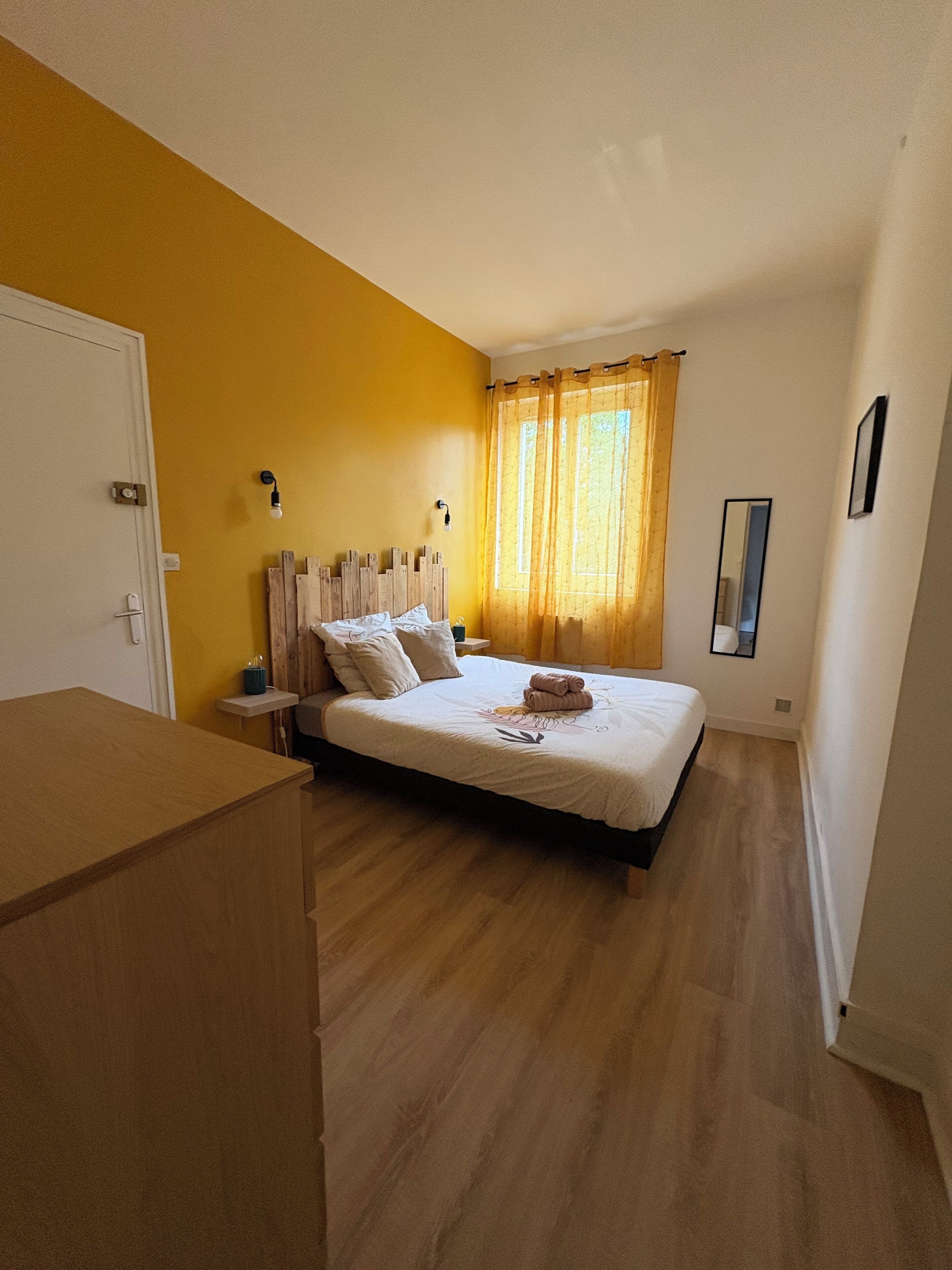 Una camera da letto con un letto, una comodino, un armadio, una finestra con tende e uno specchio a parete.