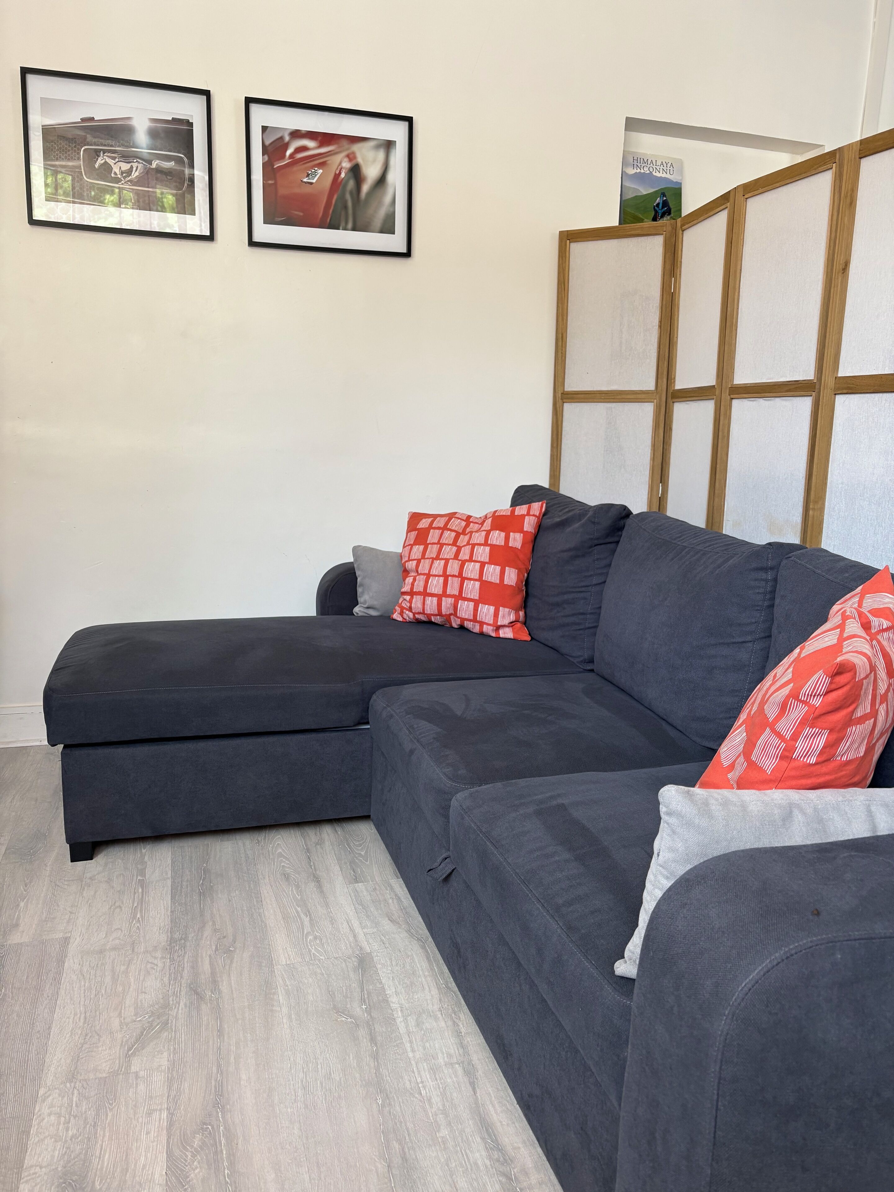 Un sofá modular con estructura de madera, suelo gris y dos cuadros enmarcados en la pared.