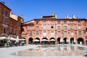 A historic building with a courtyard, featuring arches and a reflective water surface.